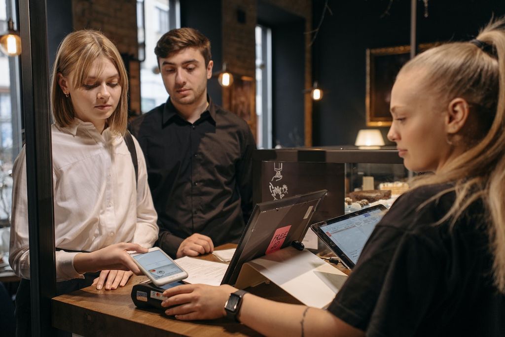 Deux clients paient avec leur smartphone en Belgique chez un commerçant qui a un terminal de paiement Bancontact compatible NFC avec une connexion internet VOObusiness