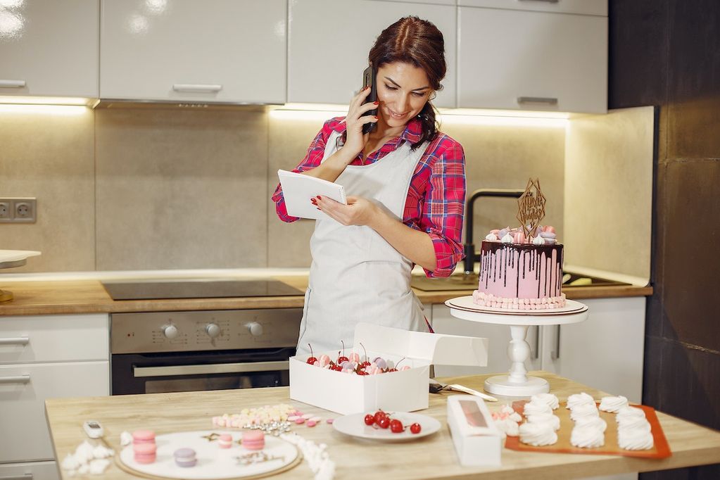 Une fille indépendante complémentaire dans sa cuisine au téléphone avec un abonnement VOObusiness mobile qui prépare des cupcakes
