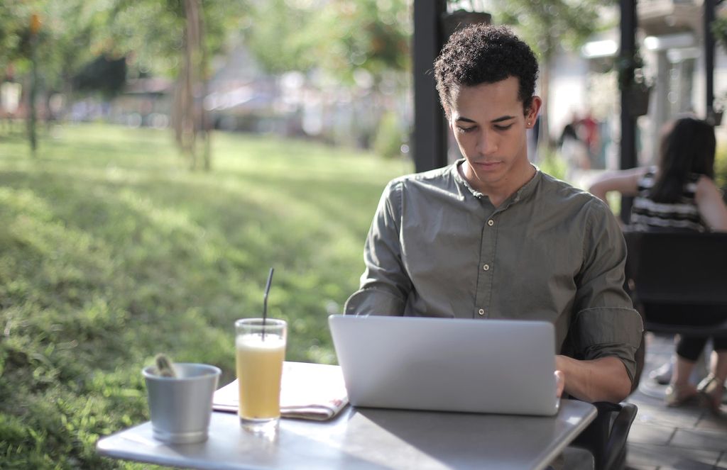 Un indépendant gère sa comptabilité à l'extérieur avec un jus sur une table et un ordinateur portable relié par hotspot wifi avec abonnement mobile VOO à 40 GB en 4G