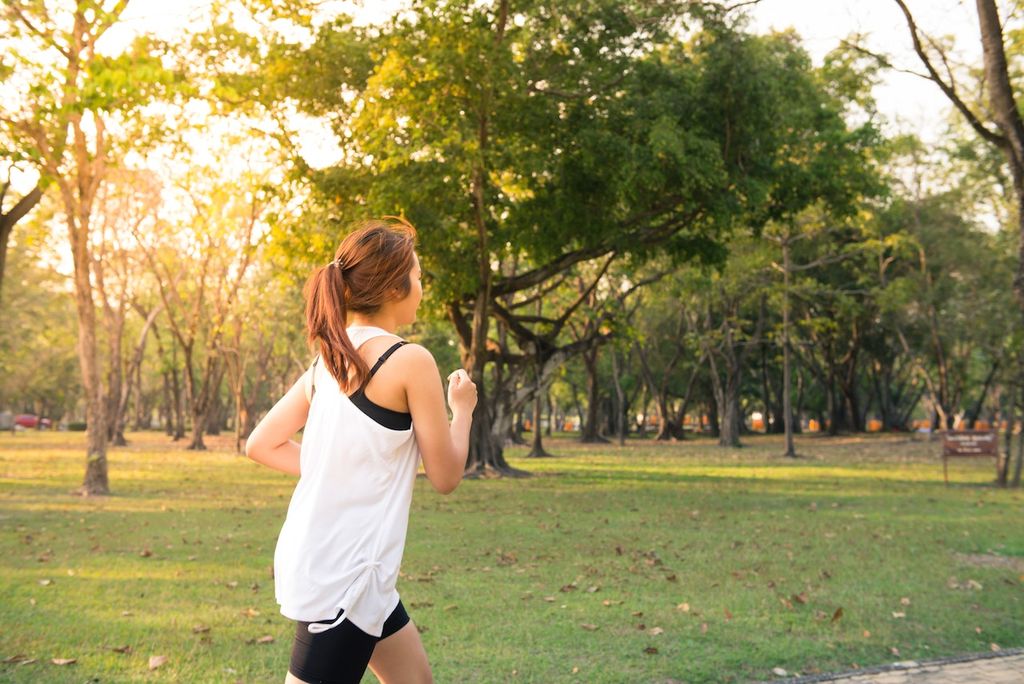 Une femme de dos fait de la course à pied dans un parc : elle prend soin d'elle-même en tant qu'indépendante