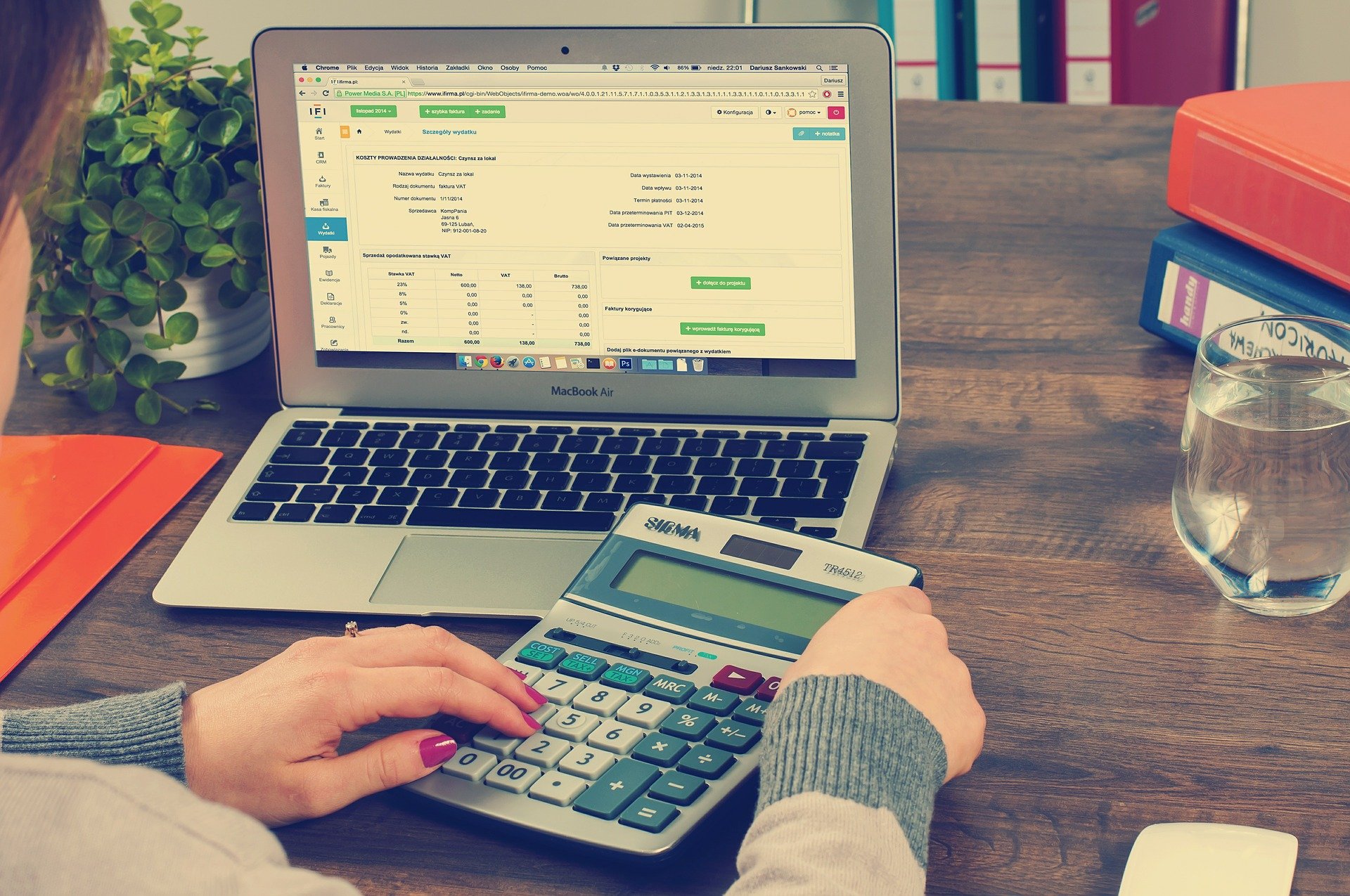 une femme utilise une calculatrice devant un Macbook pour sa comptabilité