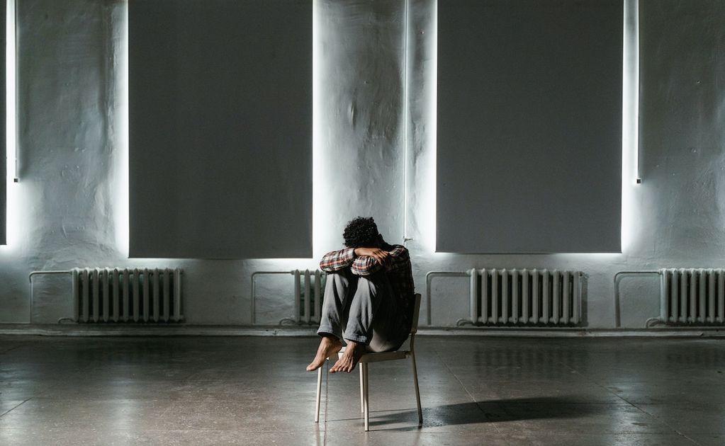 Une personne isolée et victime de cyberharcèlement au milieu d'une pièce sombre recroquevillée sur elle-même sur une chaise