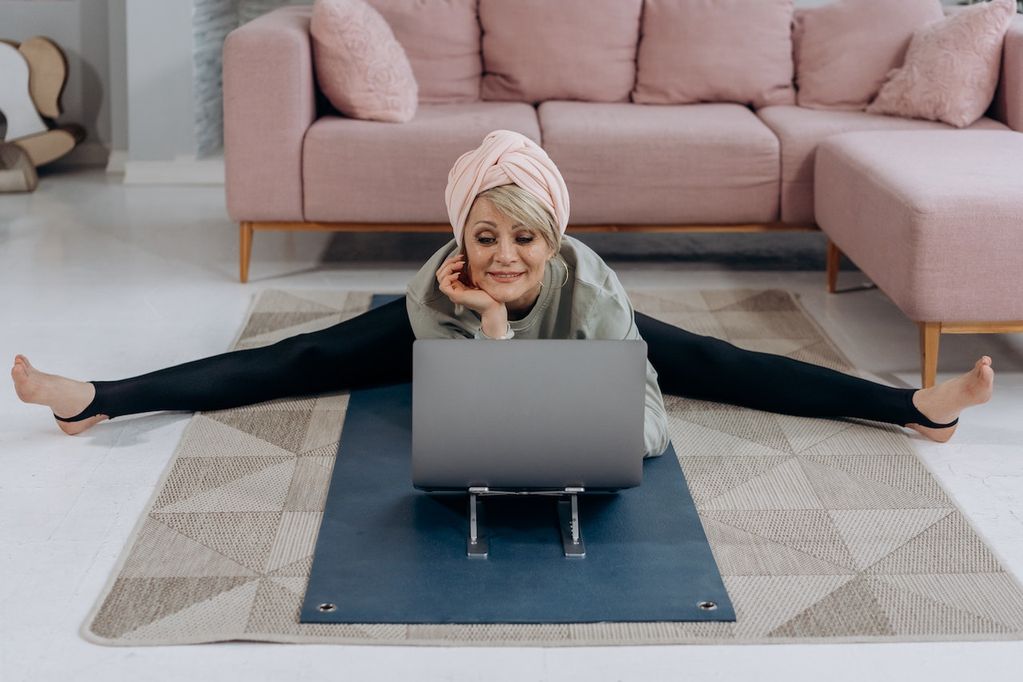Une dame fait son yoga devant son ordinateur portable et a choisi VOO pour avoir le câble et la fibre optique à la maison