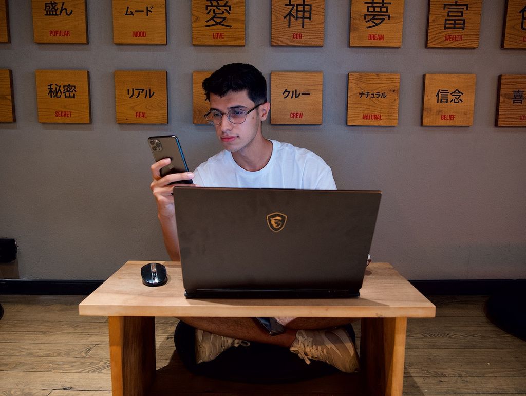 Un homme dans un bureau avec un ordinateur et un smartphone cherche les meilleurs antivirus gratuits en Belgique pour ses appareils
