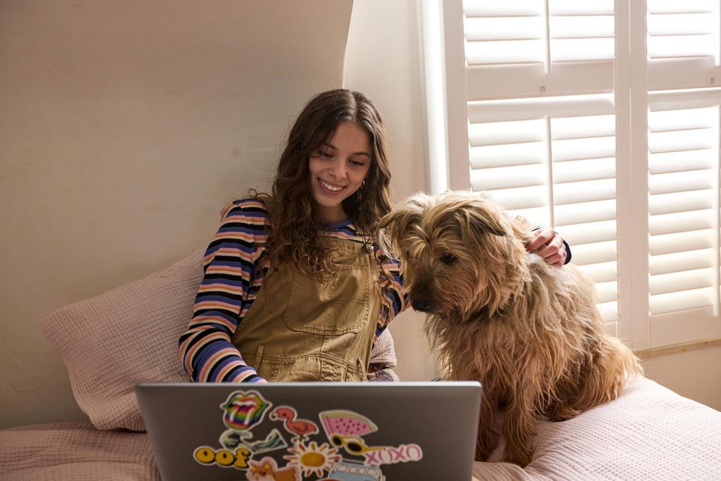 Une fille dans sa chambre avec l'internet GIGA de VOO dans une zone blanche en Wallonie elle regarde son ordinateur portable avec son chien sur son lit