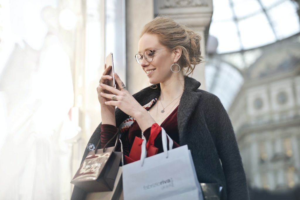 Une femme ravie de son iPhone reconditionné dans la rue, avec des sacs de shopping, l'iPhone a été acheté chez VOO en Belgique avec Recommerce