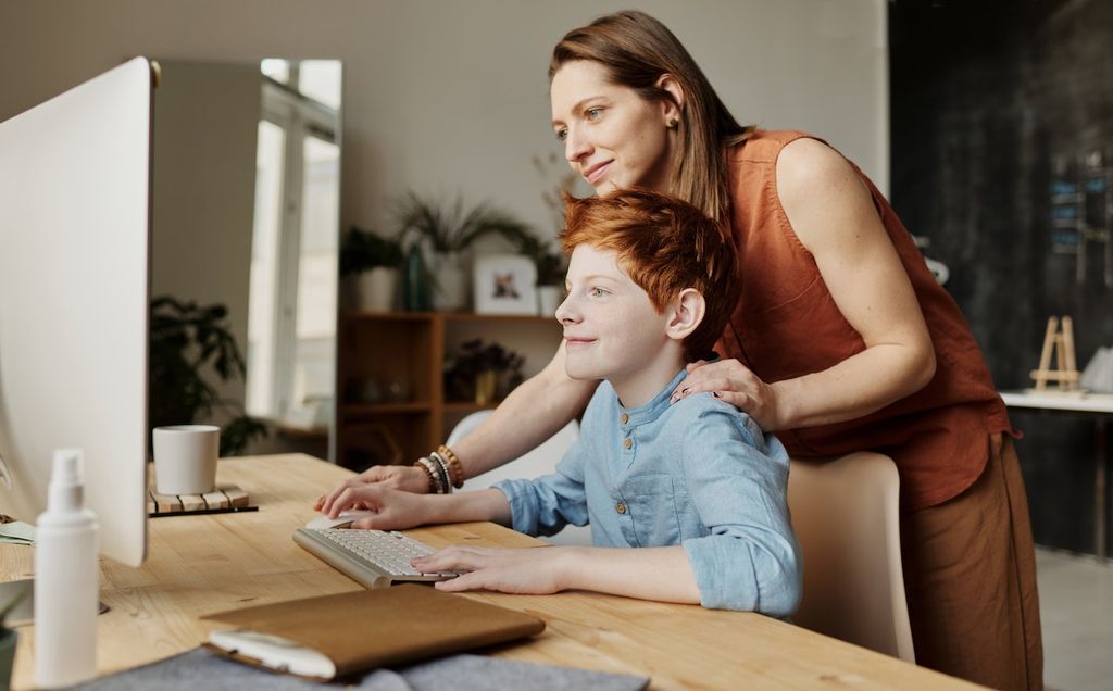 Une maman et son fils apprennent sur un ordinateur fixe à la maison en s'amusant en famille avec leur connexion internet VOO