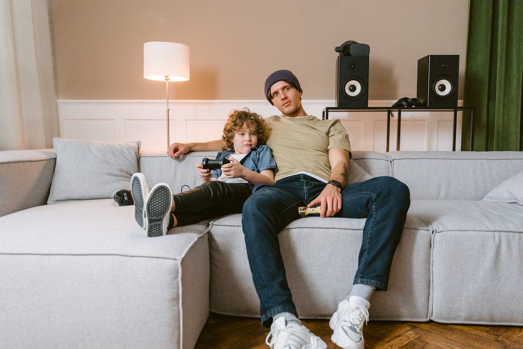 Un papa et son enfant dans le salon dans le fauteuil qui jouent aux jeux vidéo sur la Nintendo Switch