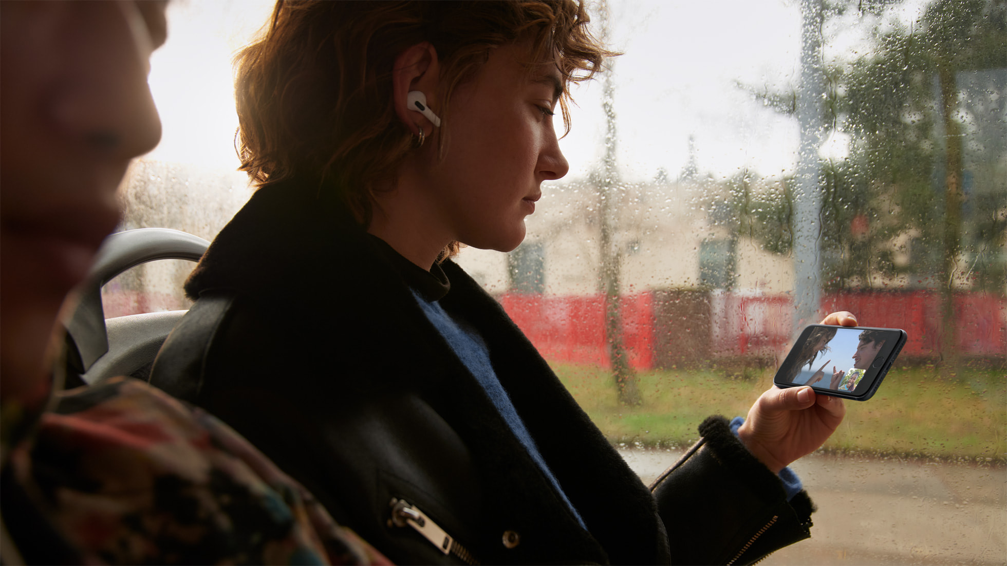 Une femme tient un iPhone SE 2022 dans les mains et regarde une vidéo avec les Airpods